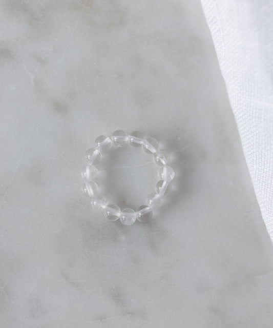 The Pop Gemstone Ring Set by WALD Berlin features a clear beaded ring with an adjustable fit, displayed on white marble beside soft fabric—perfect for unique gift ideas.