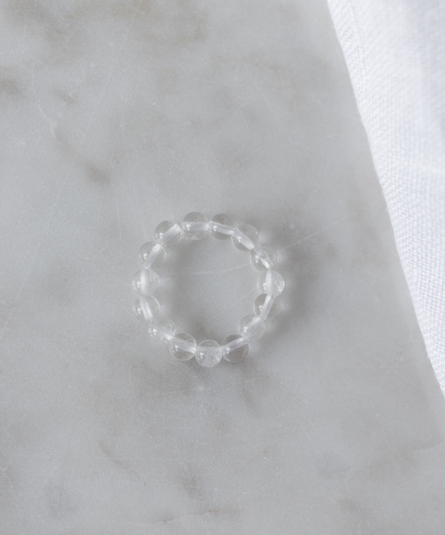 The Pop Gemstone Ring Set by WALD Berlin features a clear beaded ring with an adjustable fit, displayed on white marble beside soft fabric—perfect for unique gift ideas.