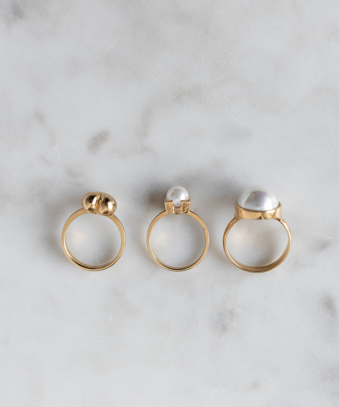 Three SAMPLE SALE Pop Pearl Rings by WALD Berlin, each with unique pearls and settings, are arranged on light marble. These elegant rings are 18k gold plated and display exquisite craftsmanship.