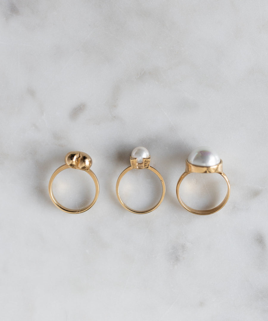 Three SAMPLE SALE Pop Pearl Rings by WALD Berlin, each with unique pearls and settings, are arranged on light marble. These elegant rings are 18k gold plated and display exquisite craftsmanship.
