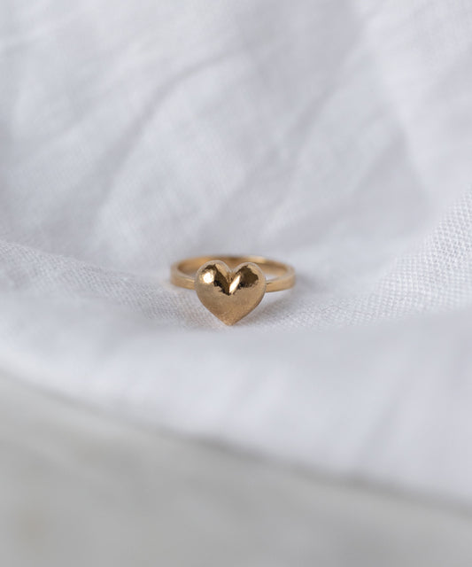 The WALD Berlin Mom Heart Ring, crafted from gold plated brass, rests on a white textured fabric background.