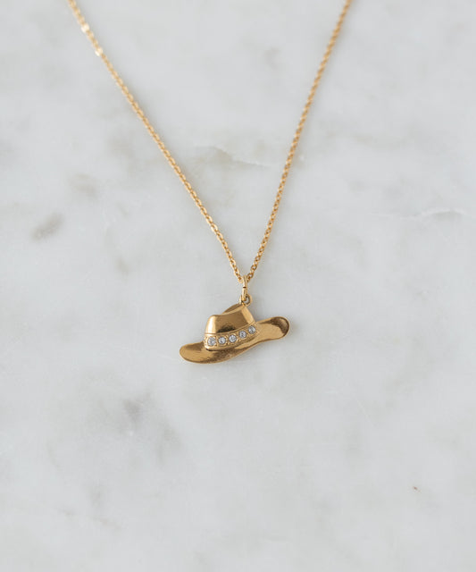 The SAMPLE SALE Pop Cowgirl Necklace by WALD Berlin is a gold necklace from Germany with a 55cm chain, featuring a cowboy hat-shaped pendant with clear gemstones, shown on white marble.