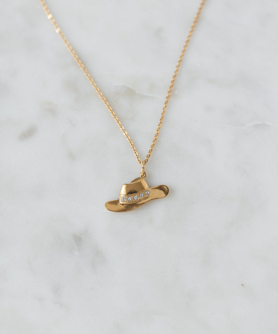 The SAMPLE SALE Pop Cowgirl Necklace by WALD Berlin is a gold necklace from Germany with a 55cm chain, featuring a cowboy hat-shaped pendant with clear gemstones, shown on white marble.