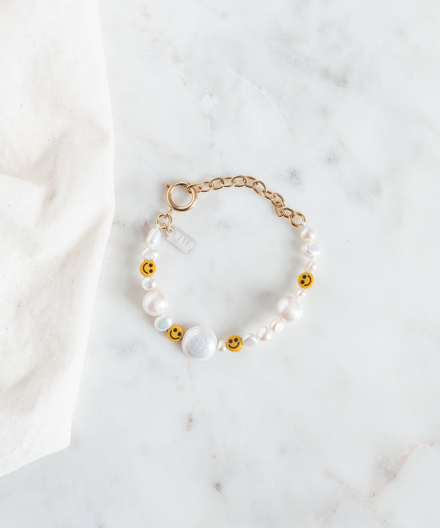 The WALD Berlin Smilie Dude Pearl Bracelet with Extention is showcased on a marble surface, featuring sweetwater pearls and cheerful smiley beads.