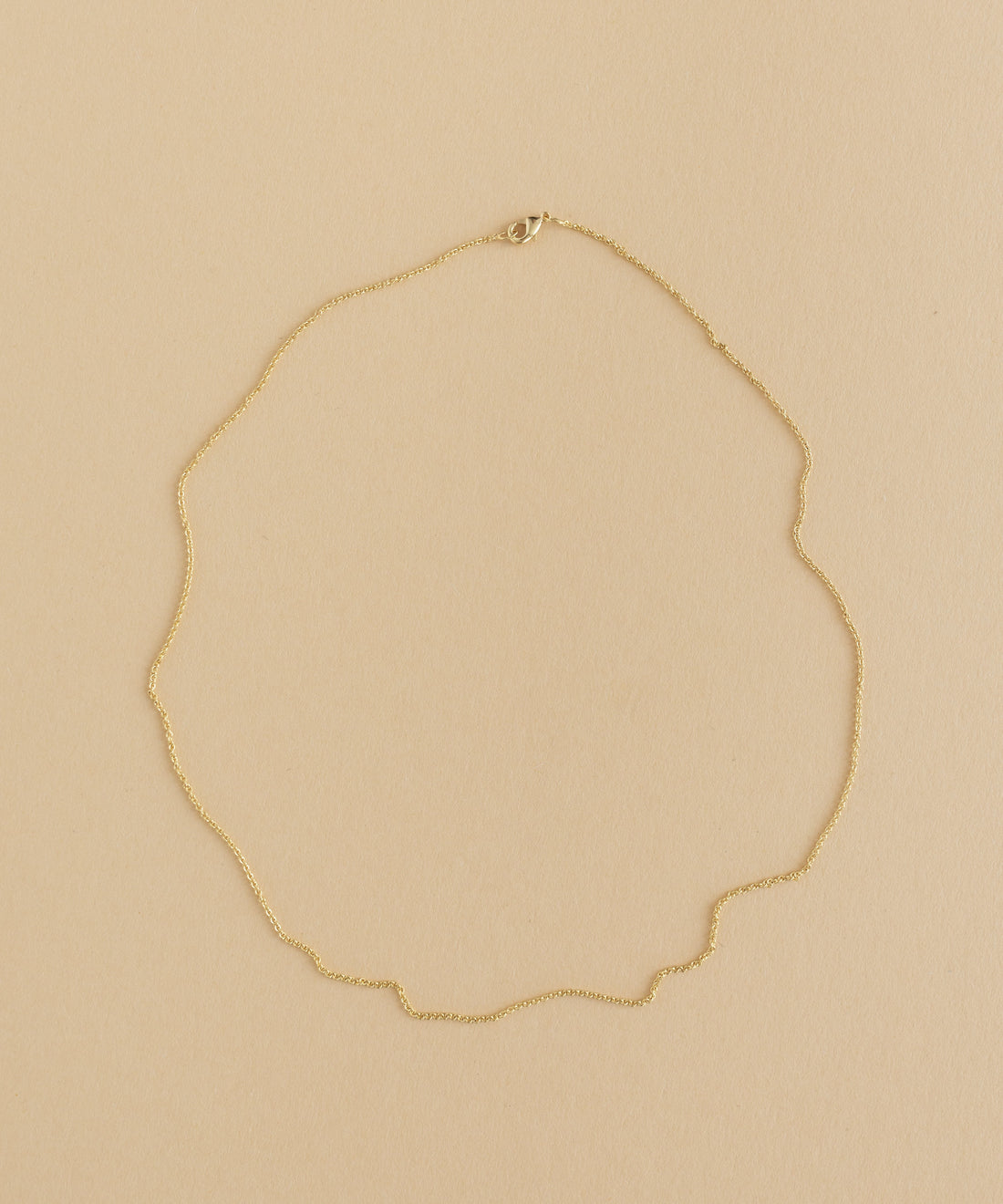 A gold necklace with a charm pendant on a beige background.