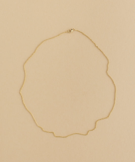 A gold necklace with a charm pendant on a beige background.