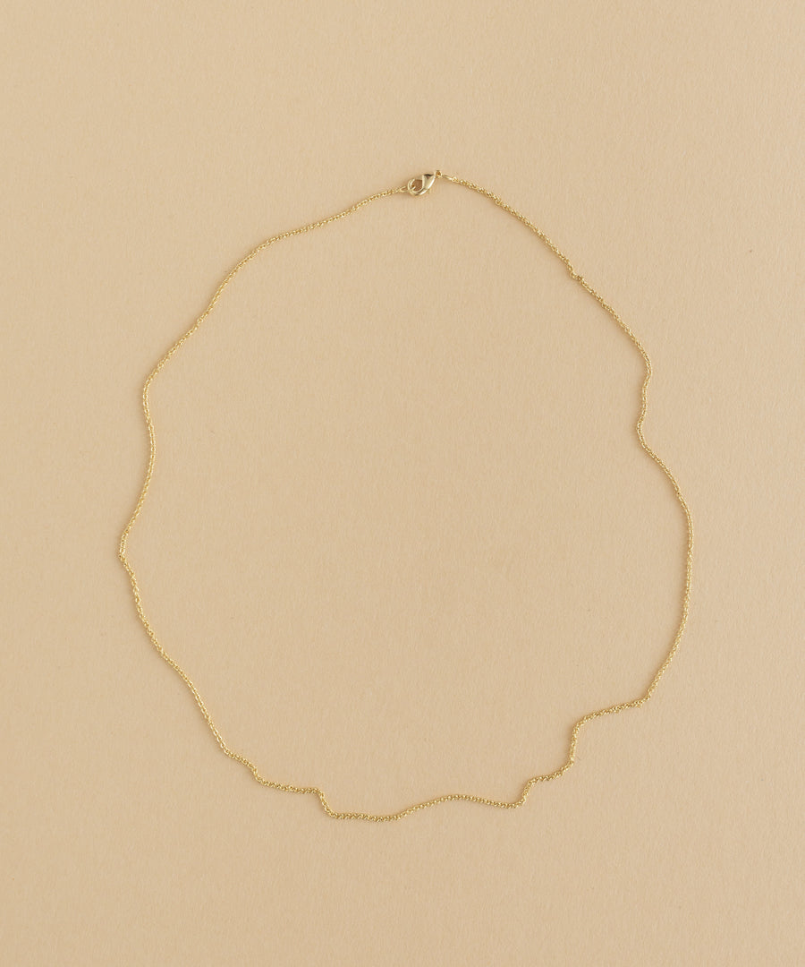 A gold necklace with a charm pendant on a beige background.