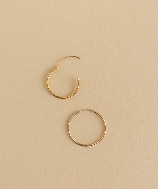 Two Gold Charm Earrings from WALD World on a beige surface.