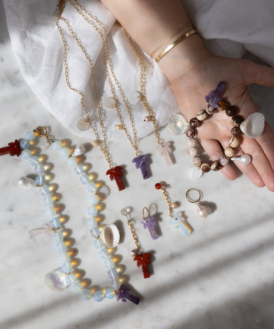 A hand displays the WALD Berlin Mexicana La Bamba Bracelet, while more chunky bracelets, necklaces, and earrings are arranged on a marble surface.