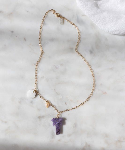 Die WALD Berlin Mexicana Solo Amore Halskette ist ein handgefertigtes, vergoldetes Stück mit einem violetten Steinanhänger, einem runden weißen Charm und einer kleinen Perle, die elegant auf weißem Marmor präsentiert werden.