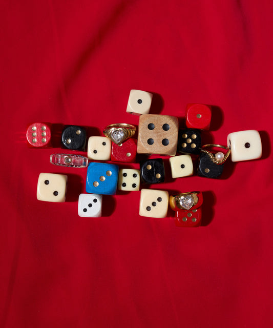 A mix of colorful dice in different sizes, some topped with WALD Berlin’s NYC If I Rule The World Ring, handmade from recycled gold in Germany, displayed on a red fabric background.