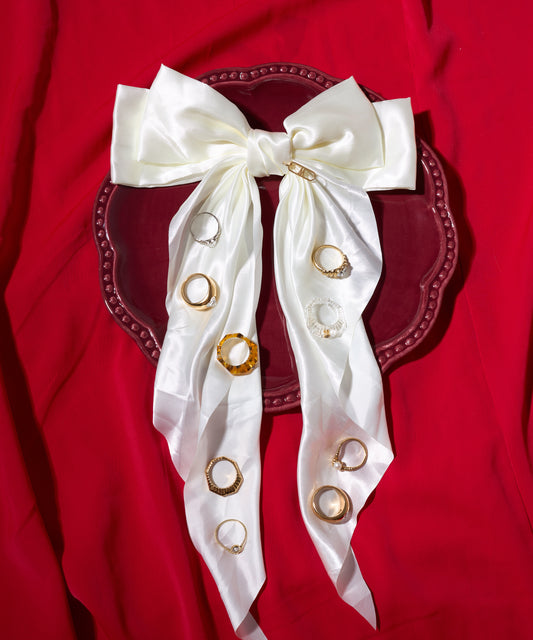 The WALD Berlin NYC If I Rule The World Ring, handmade in Germany, is shown on a maroon plate with a white satin bow and gold-plated accents, set against a red fabric background.