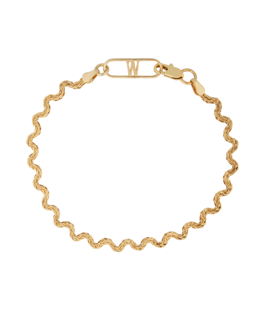 The Irina Gold Bracelet by WALD Berlin is an expertly crafted 18k gold bracelet featuring a wavy chain design and a rectangular clasp with the letter "W" on a black background, made in Germany.