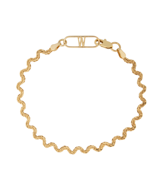 The Irina Gold Bracelet by WALD Berlin is an expertly crafted 18k gold bracelet featuring a wavy chain design and a rectangular clasp with the letter "W" on a black background, made in Germany.