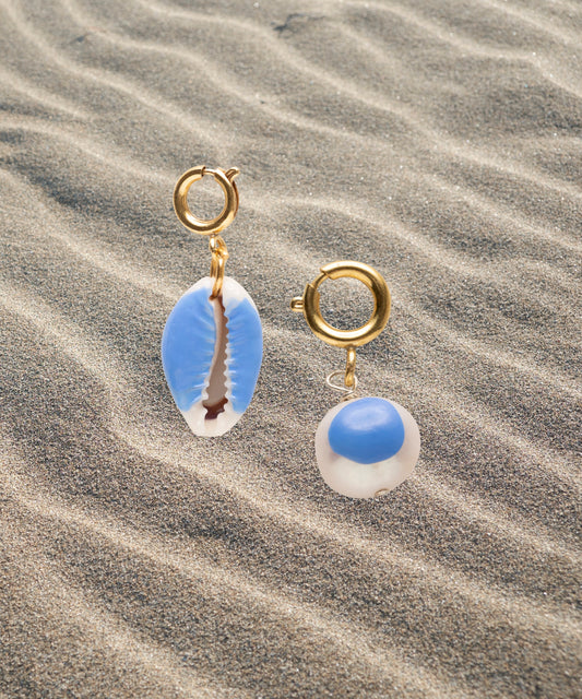 The WALD Berlin SAMPLE SALE Beach Babe Charms feature two gold hoop earrings with blue and white shell pendants and sweetwater pearl accents, styled on rippled sand.