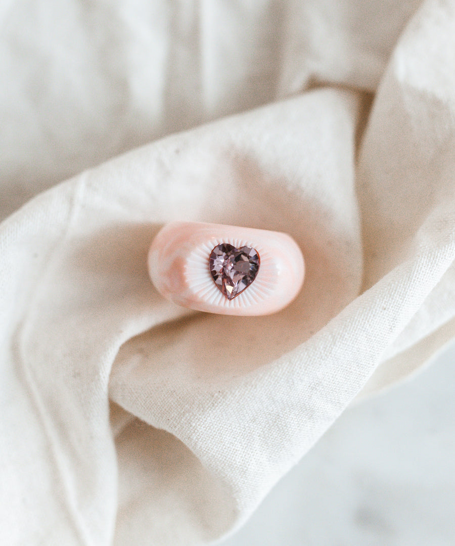 A love-inspired pink heart-shaped WALD x Zeena Rose Heart Ring on a white cloth. (Brand: WALD Berlin)