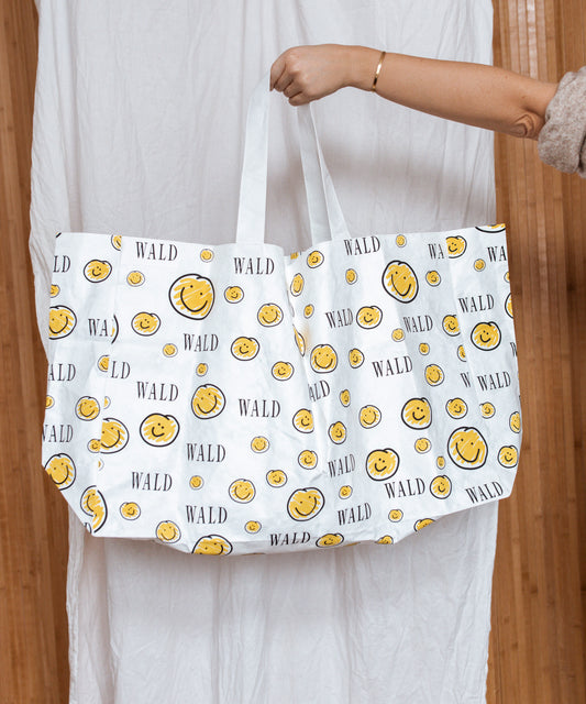 A woman holding a smiley face adorned WALD Berlin shopper bag, showcasing Germany's fashionable jewelry capital.