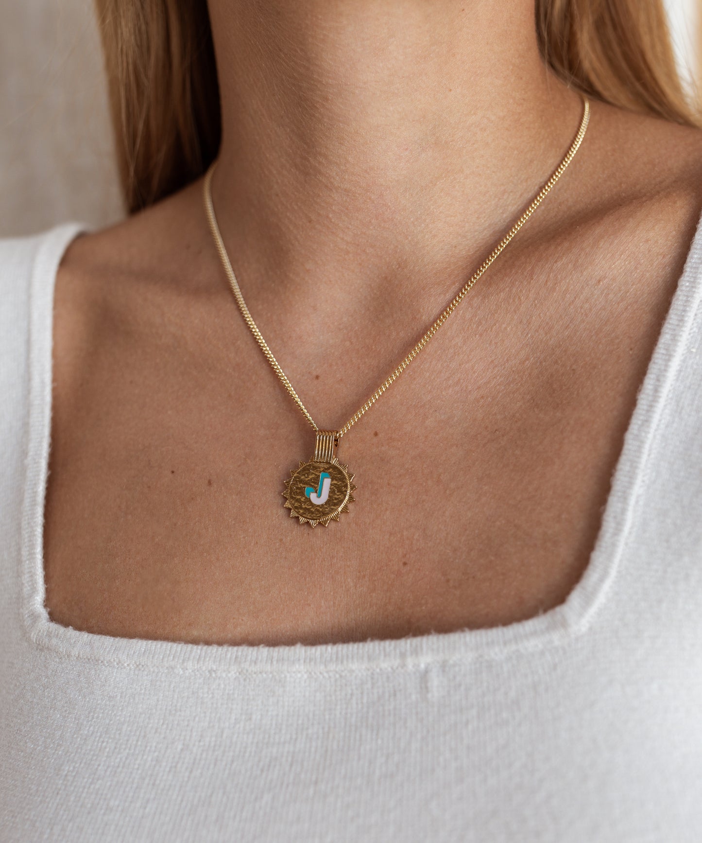 A woman wears the WALD Berlin Sample saleSay My Name Gold Necklace, featuring a gold-plated round pendant with a blue "J" initial and adjustable chain, styled with a white square-neck top.