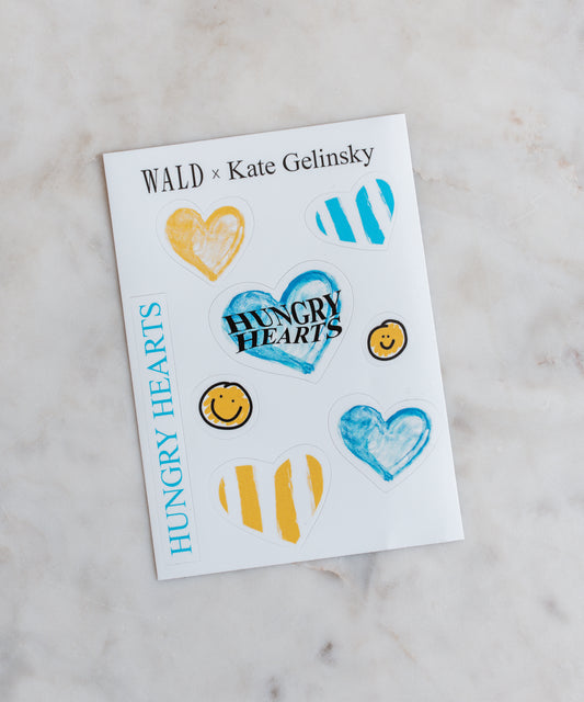 WALD Berlin presents the WALD x Kate Gelinsky Sticker Sheet, showcasing watercolor hearts and smiley faces along with the text "HUNGRY HEARTS." This collaboration pairs seamlessly with their exclusive heart necklace jewelry.