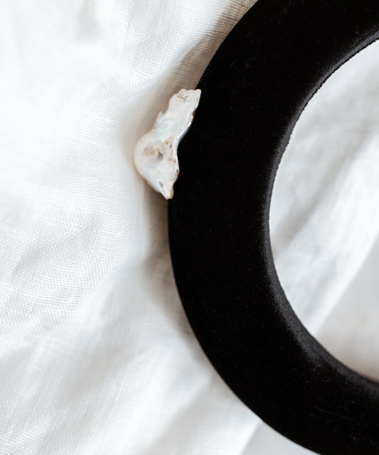 The SAMPLE SALE Baroque Pearl Black Headband by WALD Berlin features a single baroque pearl on black velvet, displayed against a white fabric background. Made in Germany.