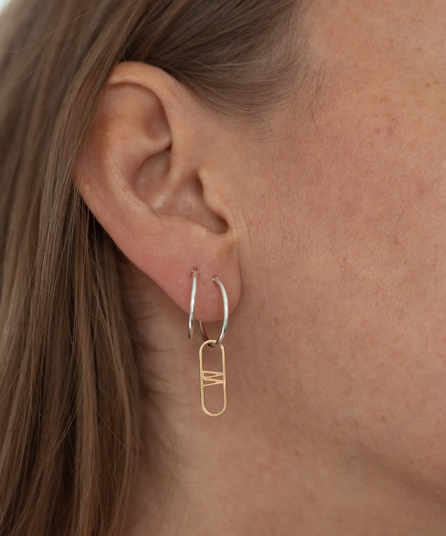 Close-up of a person's ear wearing the SAMPLE SALE NYC Cream Earrings by WALD Berlin, featuring hand-made sterling silver hoops each adorned with a gold geometric charm.