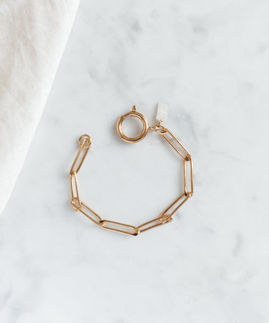 The WALD Berlin SAMPLE SALE Ashley Gold Bracelet, featuring elongated gold-plated links and a round clasp, is displayed on a light marble surface.