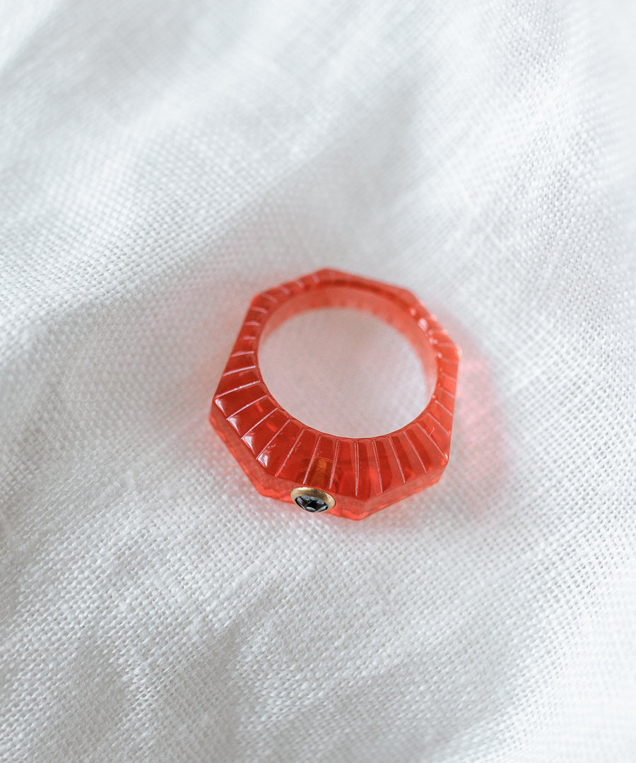 The SAMPLE SALE Shining Star Red Ring by WALD Berlin features a faceted, translucent red octagonal design with a small metal stud and Swarovski stone, displayed atop white textured fabric.