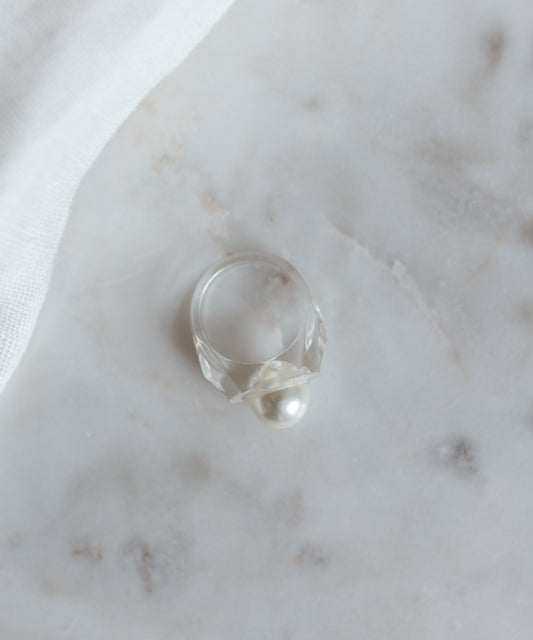 The WALD Berlin Happy No No No Ring SAMPLE, with its translucent band and Swarovski pearl, adorns a marble surface partially covered by white fabric.