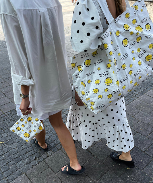 Two Berlin women flaunting jewelry while walking down the street with WALD Berlin Smilie Dude Shopper bags.