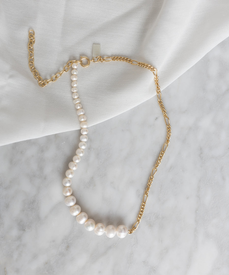 A Berlin-inspired Pas De Deux Necklace by WALD with a gold chain showcased on a marble table.